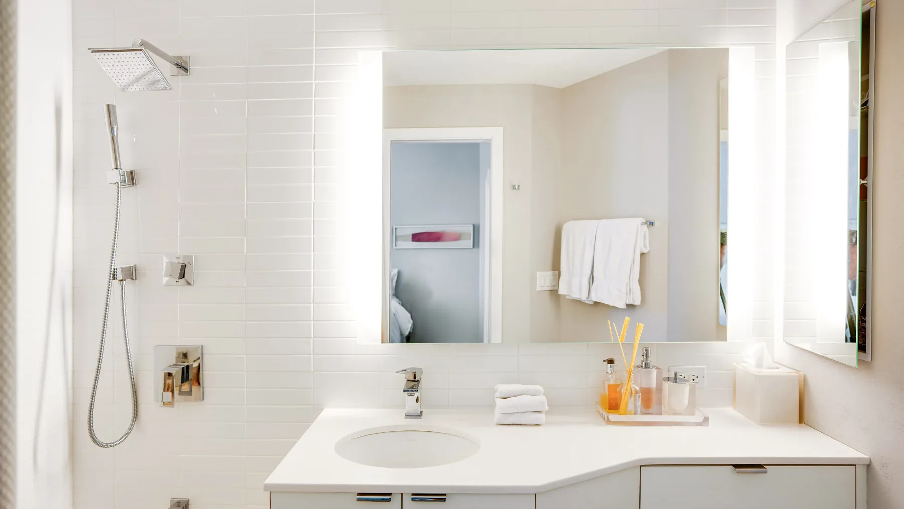 A bright bathroom with a sink, mirror, and wall-mounted shower.