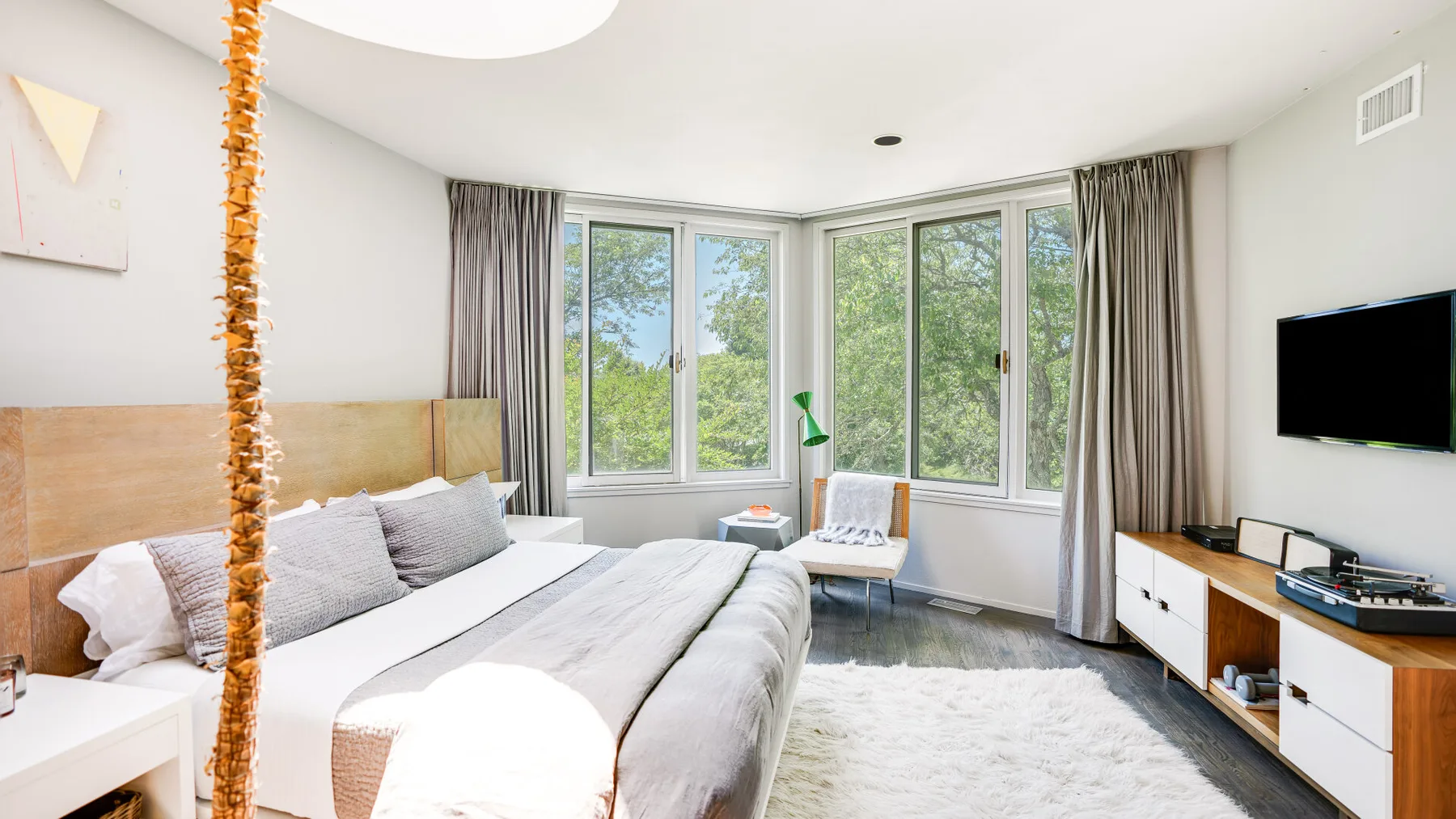 A bright bedroom with a bed, a large window, and a television.