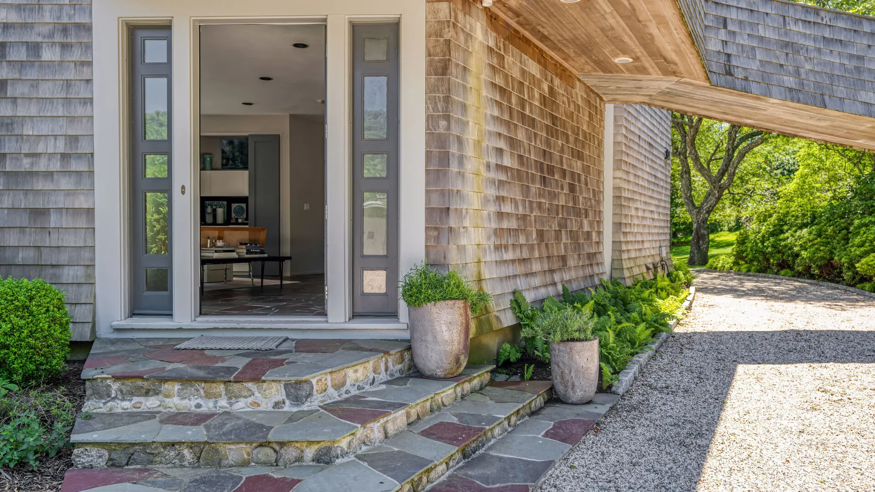 An open entrance with tall glass panels leads into a room, beside a gravel driveway.