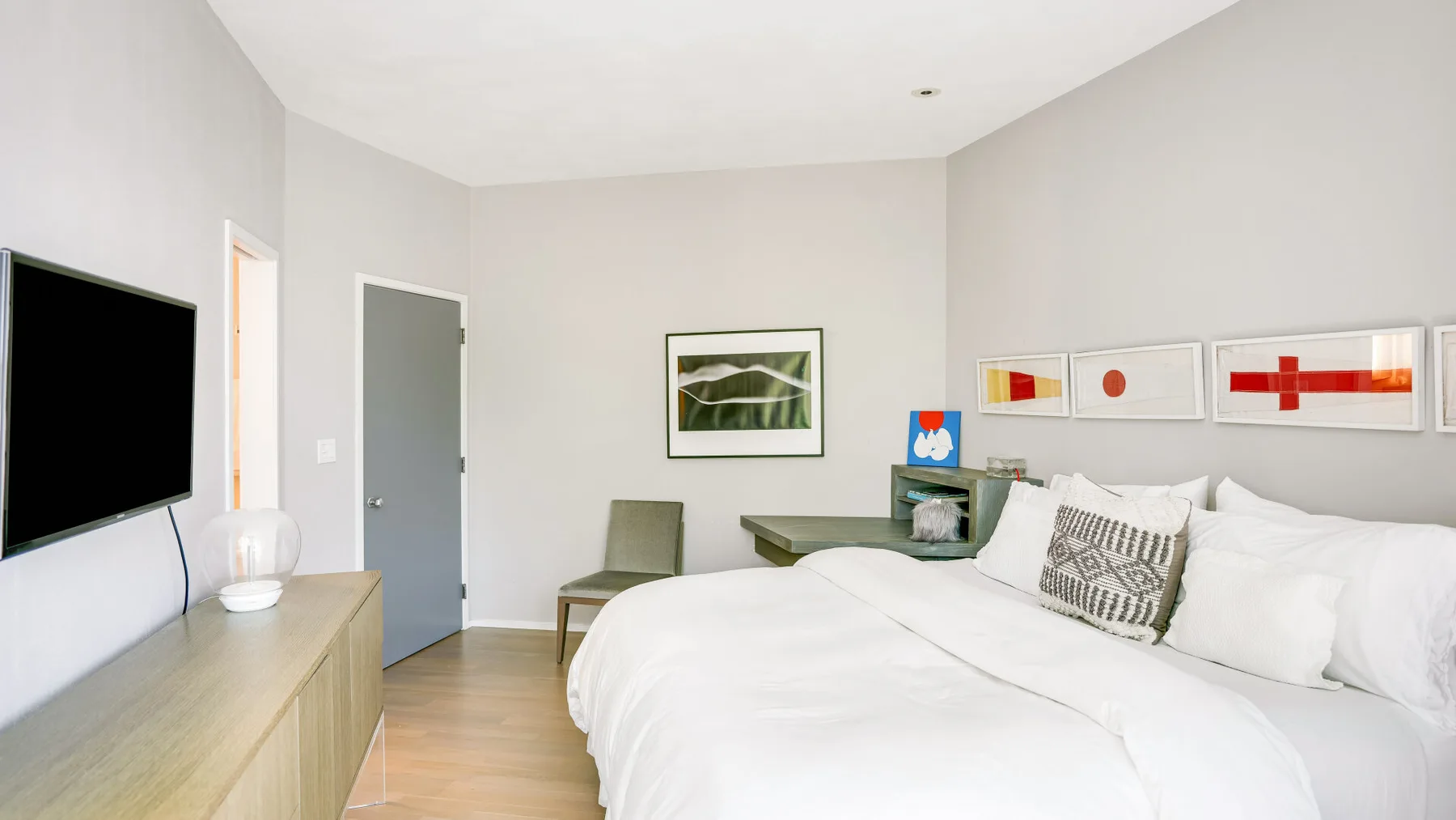 A bright bedroom with a large bed, wall-mounted television, and framed artwork.