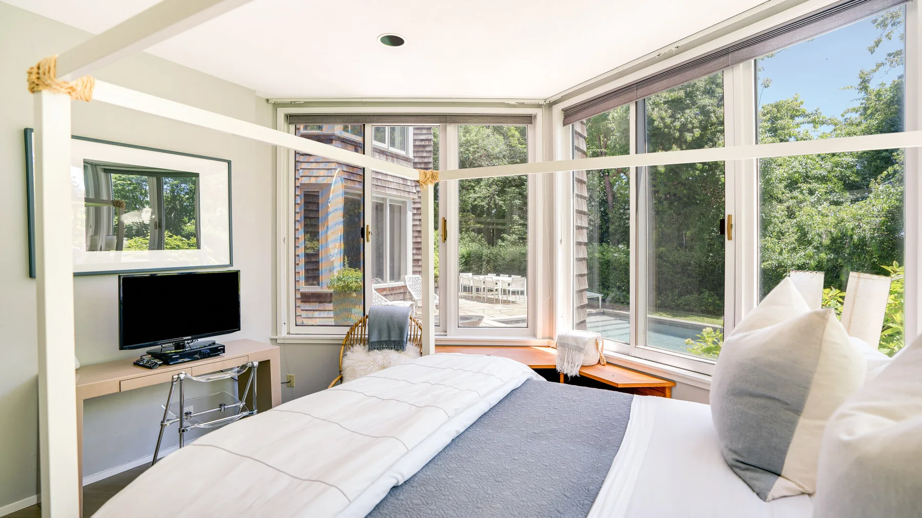 A bright bedroom with a bed beside large windows overlooking a garden.
