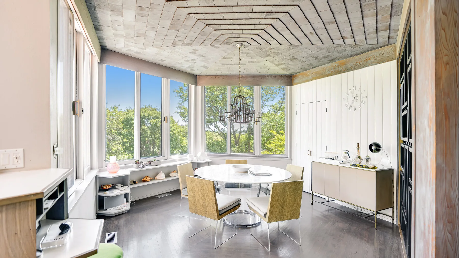 A bright dining area has a round table beside large windows and built-in seating.