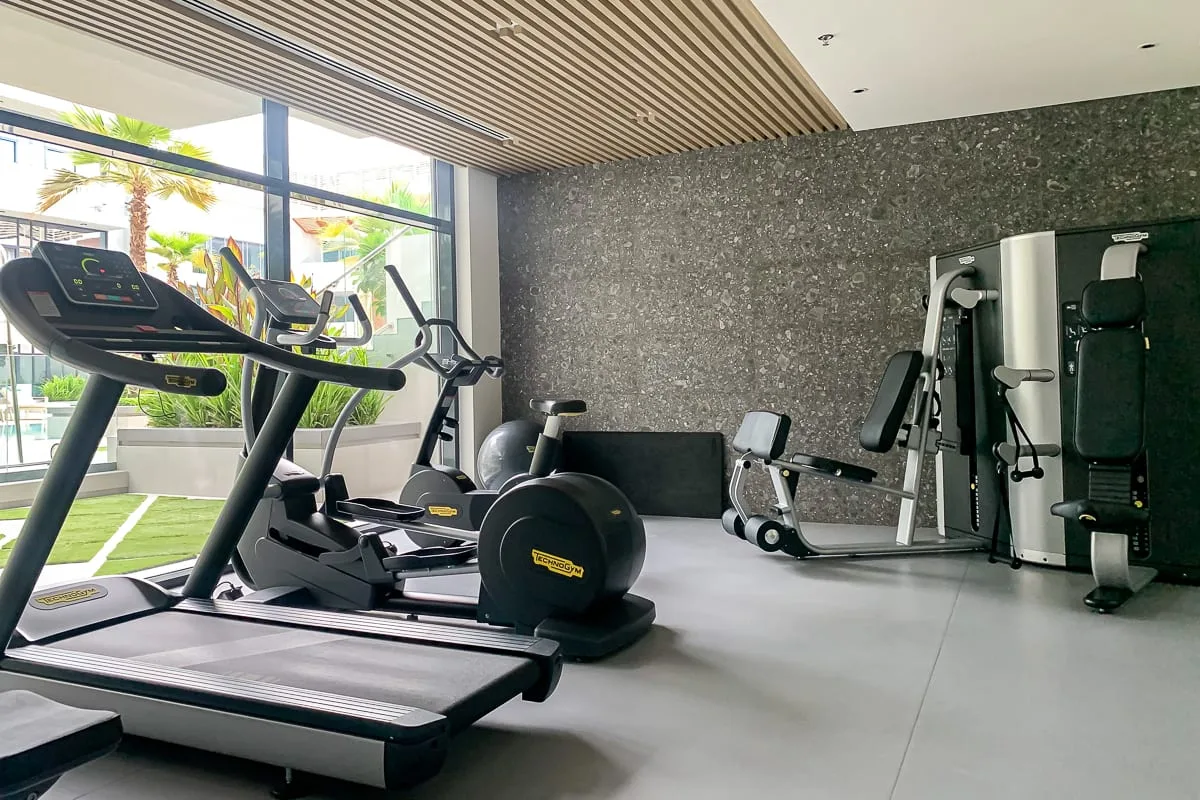 Una sala de fitness con cintas de correr y máquinas de ejercicio junto a grandes ventanales.