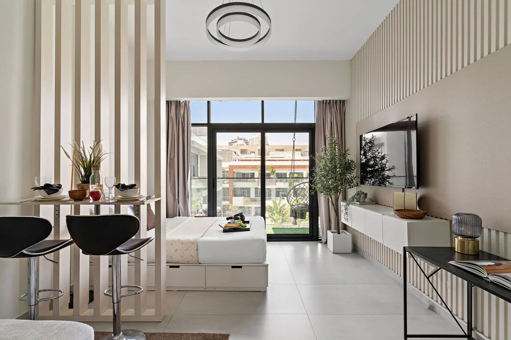 Una sala luminosa con televisión, asientos y puertas de vidrio que dan a un balcón.