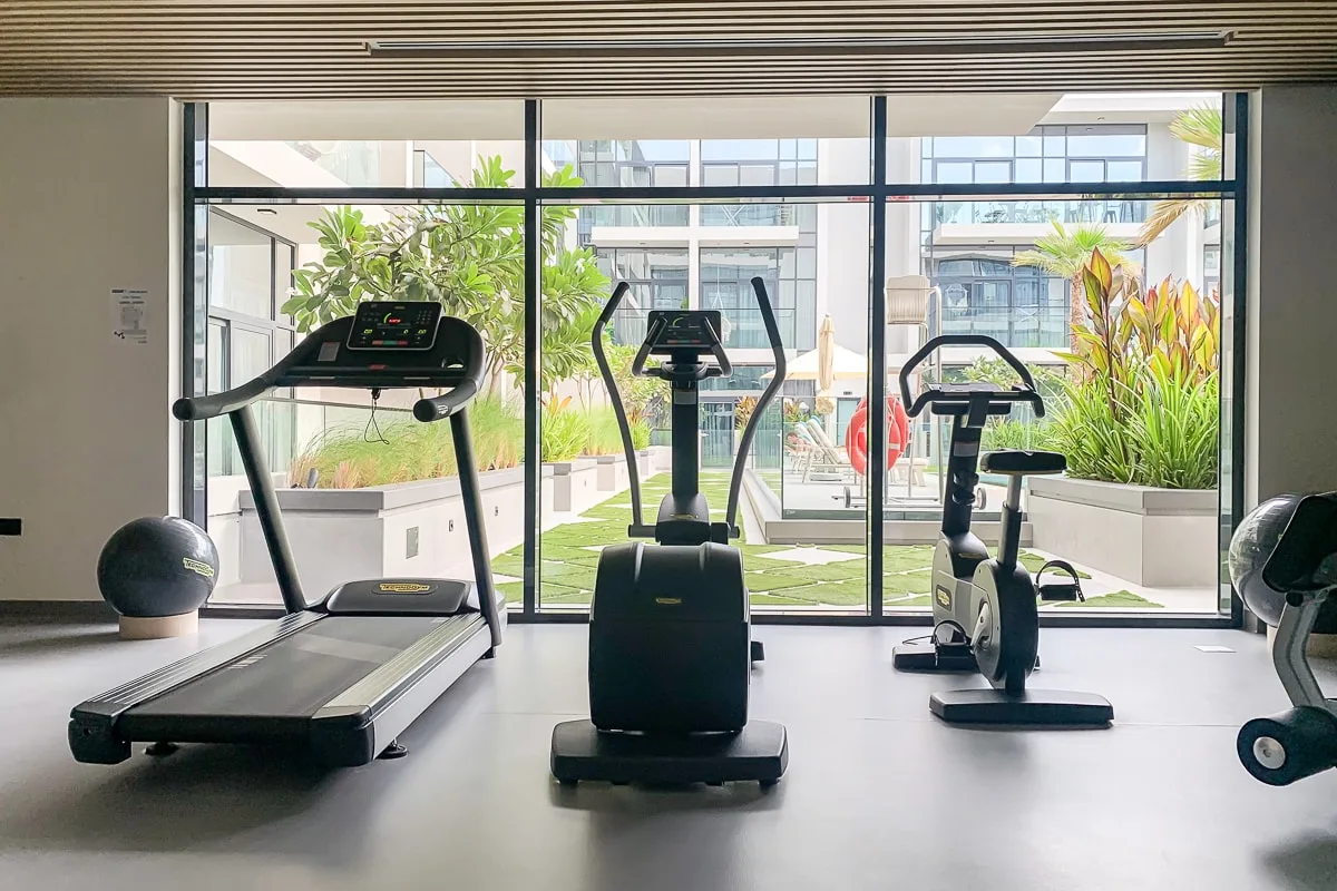 Un gimnasio con equipos cardiovasculares junto a ventanas de piso a techo.
