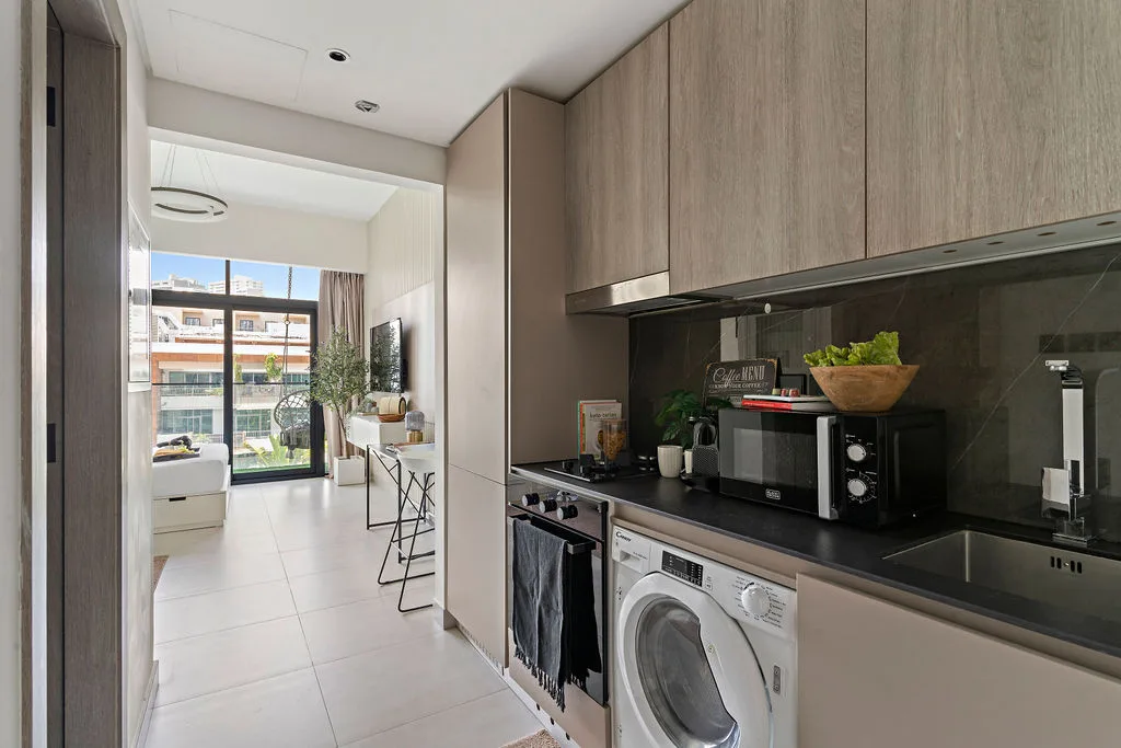 Una cocina moderna con lavadora y encimera se abre a una luminosa sala de estar.