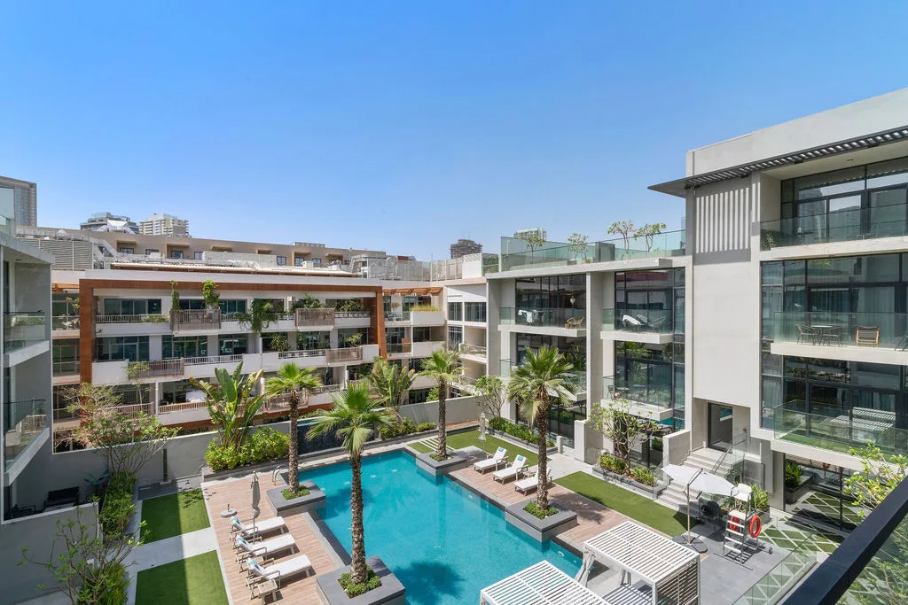 Una piscina exterior ajardinada está rodeada de edificios modernos y palmeras.