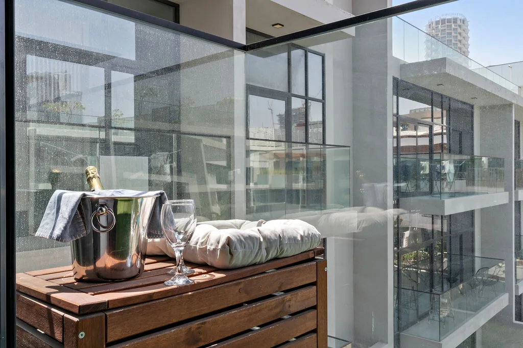 Una zona de estar en un balcón con mesa de madera, copas y cojines doblados.