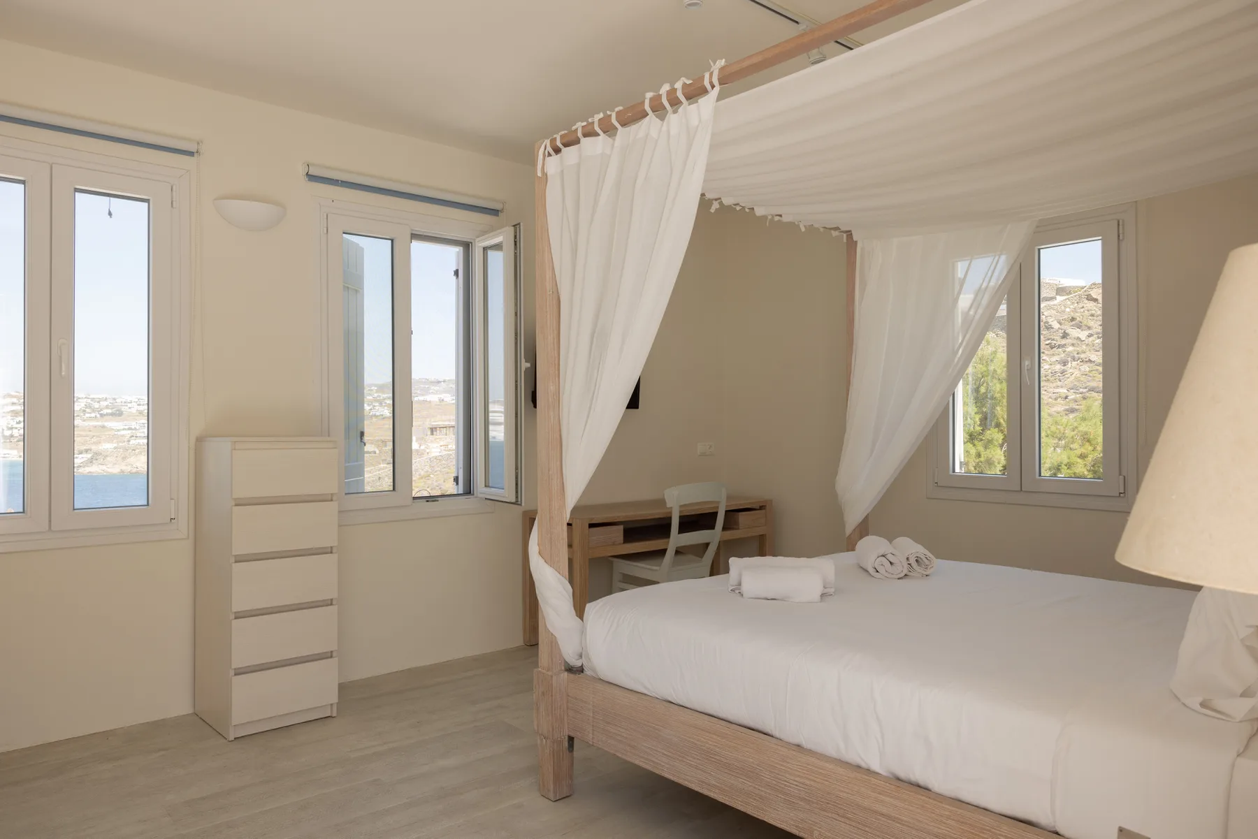 A bright bedroom with a white canopy bed and several windows.