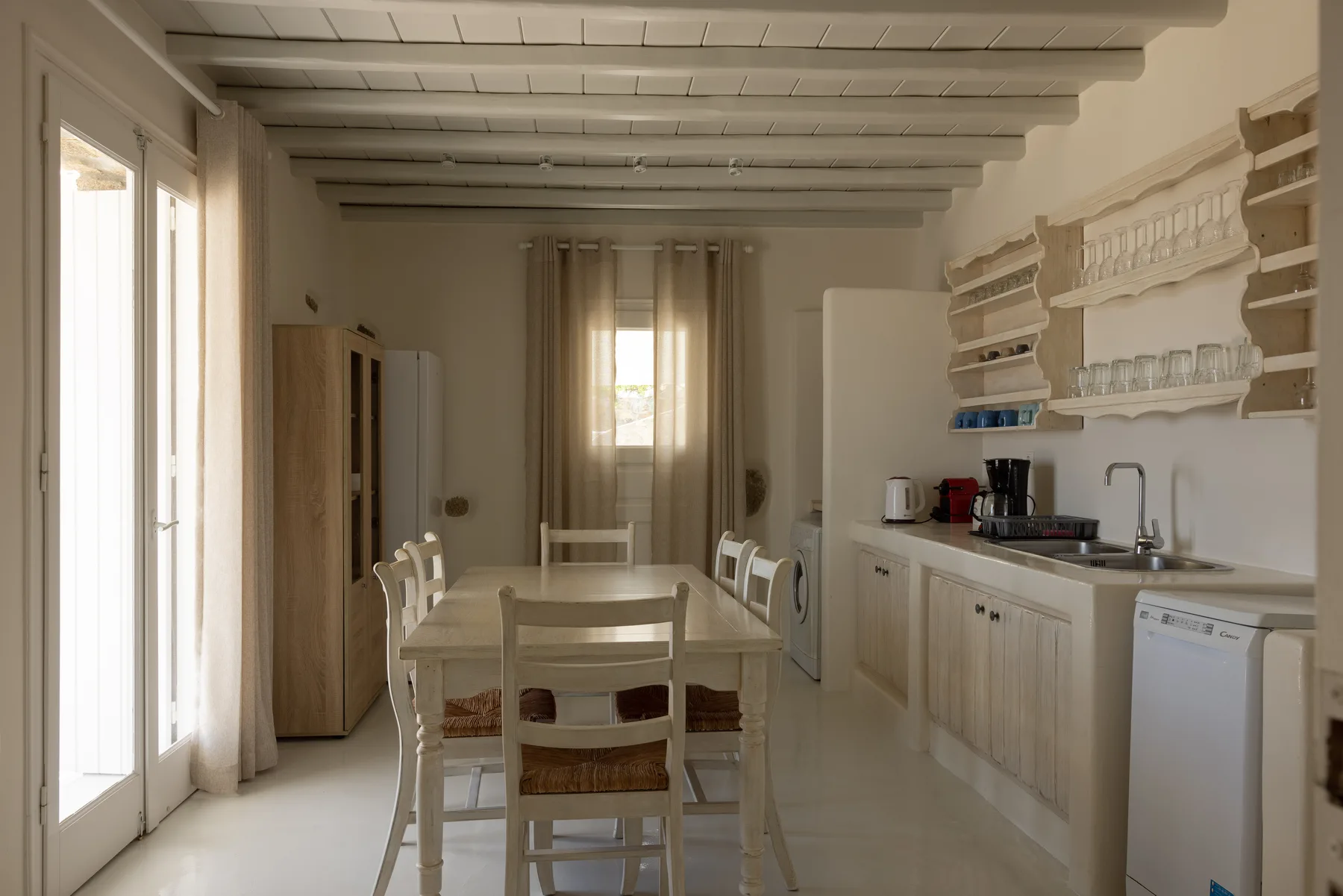 A dining table and chairs sit beside a compact kitchen with open shelves.
