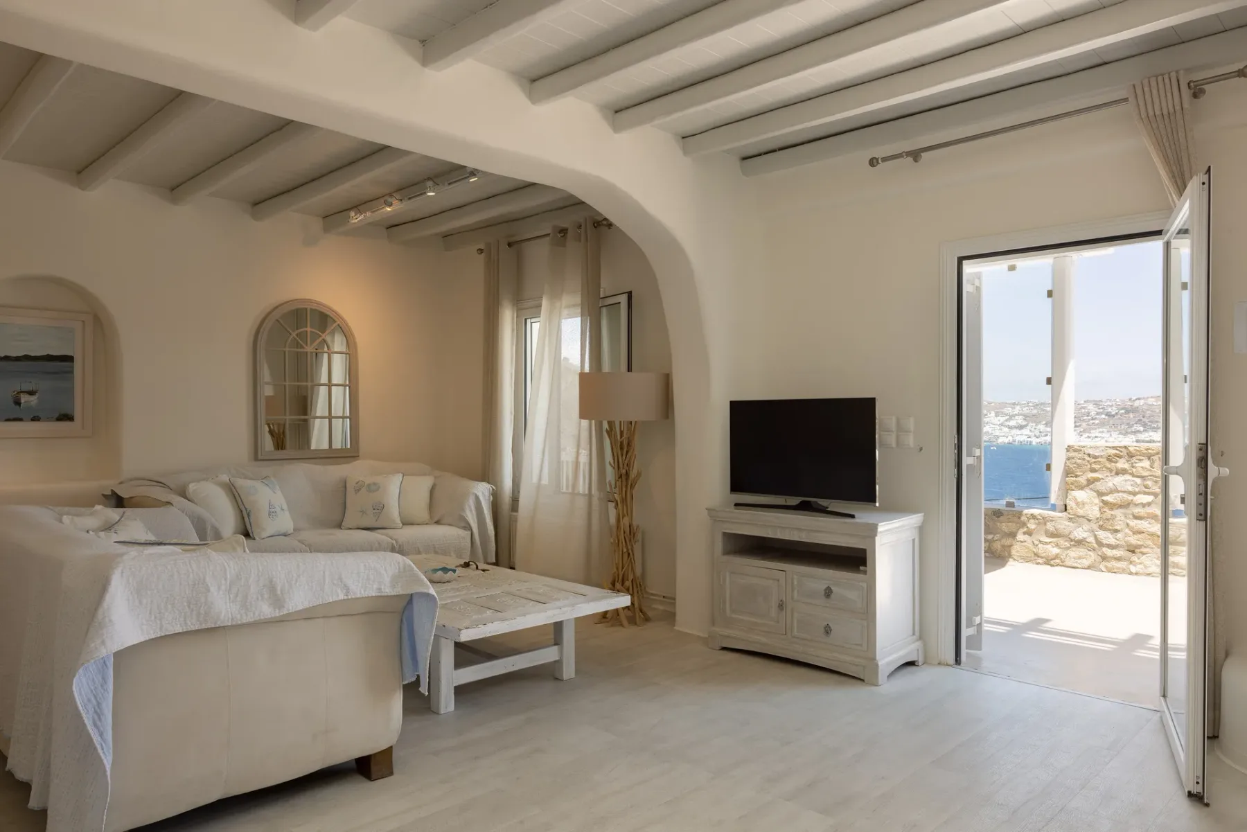 A bright living room with seating, a television, and an open doorway to a sunlit terrace.