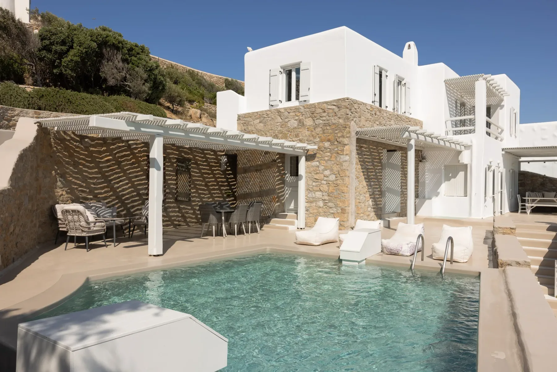 A modern white house overlooks a swimming pool with shaded outdoor seating.