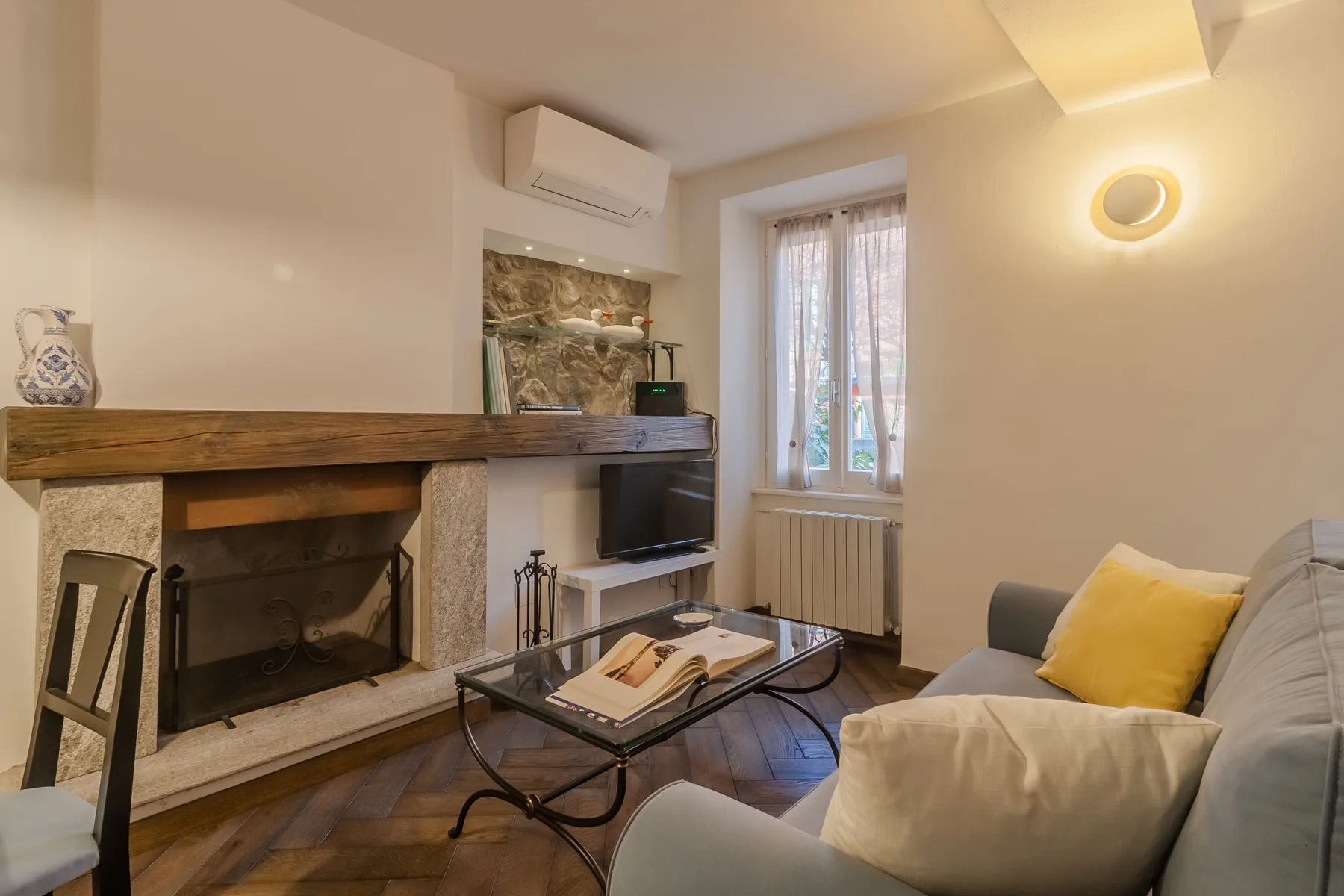 A living room with a fireplace, seating, and a television beside a window.