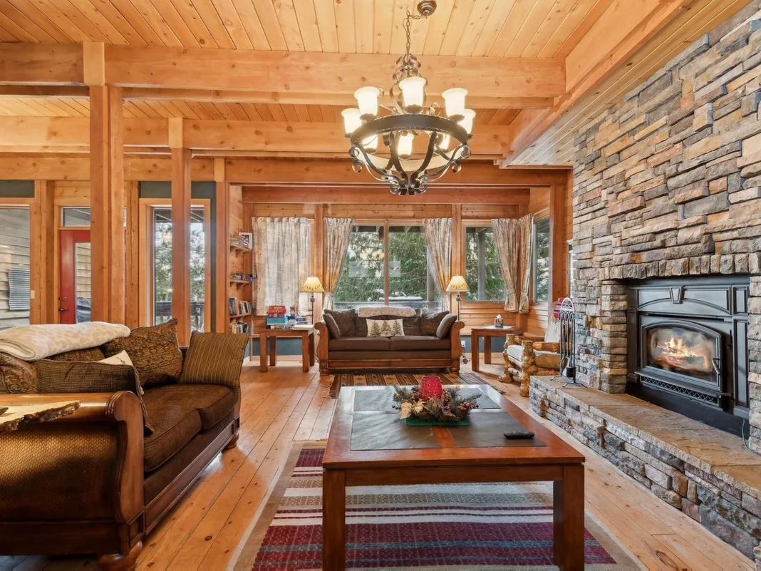 A wood-paneled living room with seating, a coffee table, and a stone fireplace.