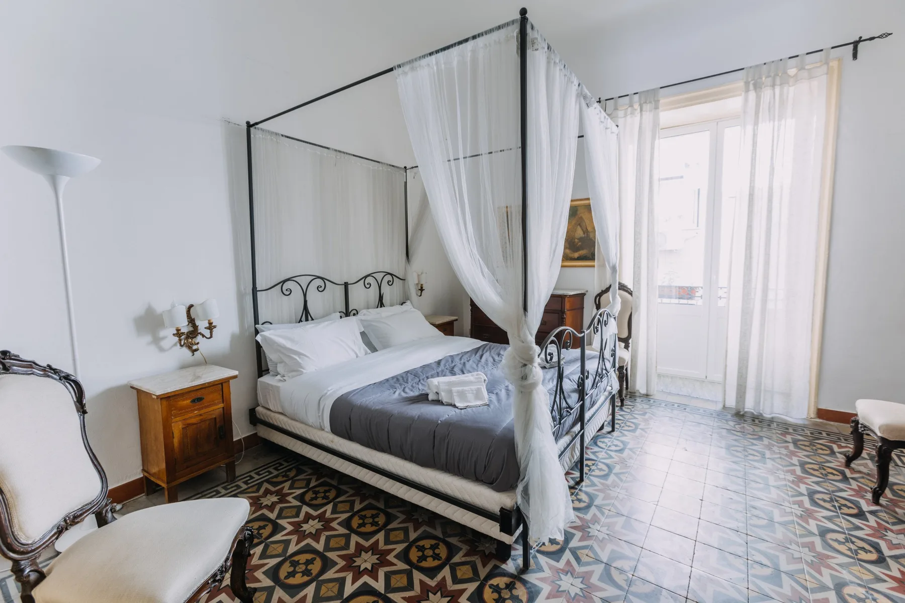 Dormitorio con una cama con dosel y cortinas, y suelo de baldosas estampadas.