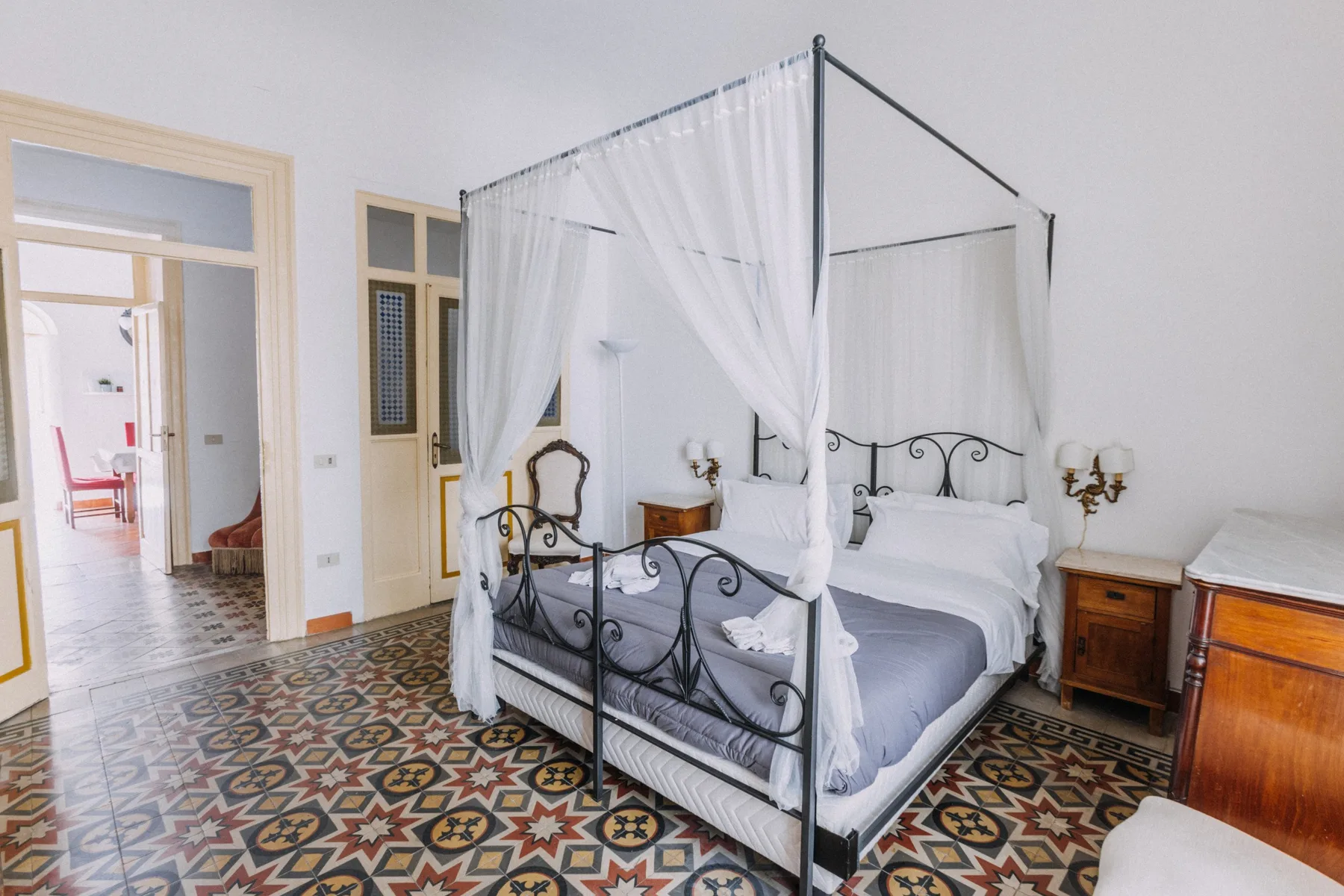 Un dormitorio con cama con dosel, mesitas de noche y suelo de baldosas estampadas.