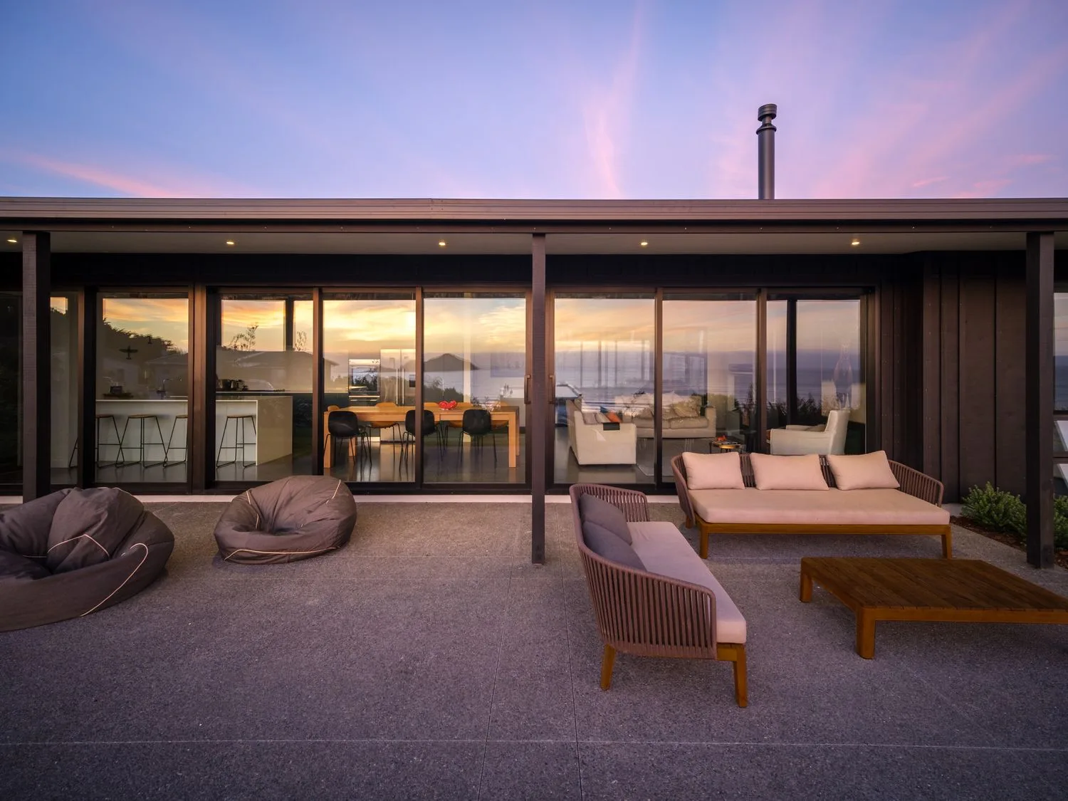An outdoor patio with cushioned seating and a low table faces a house with glass doors.