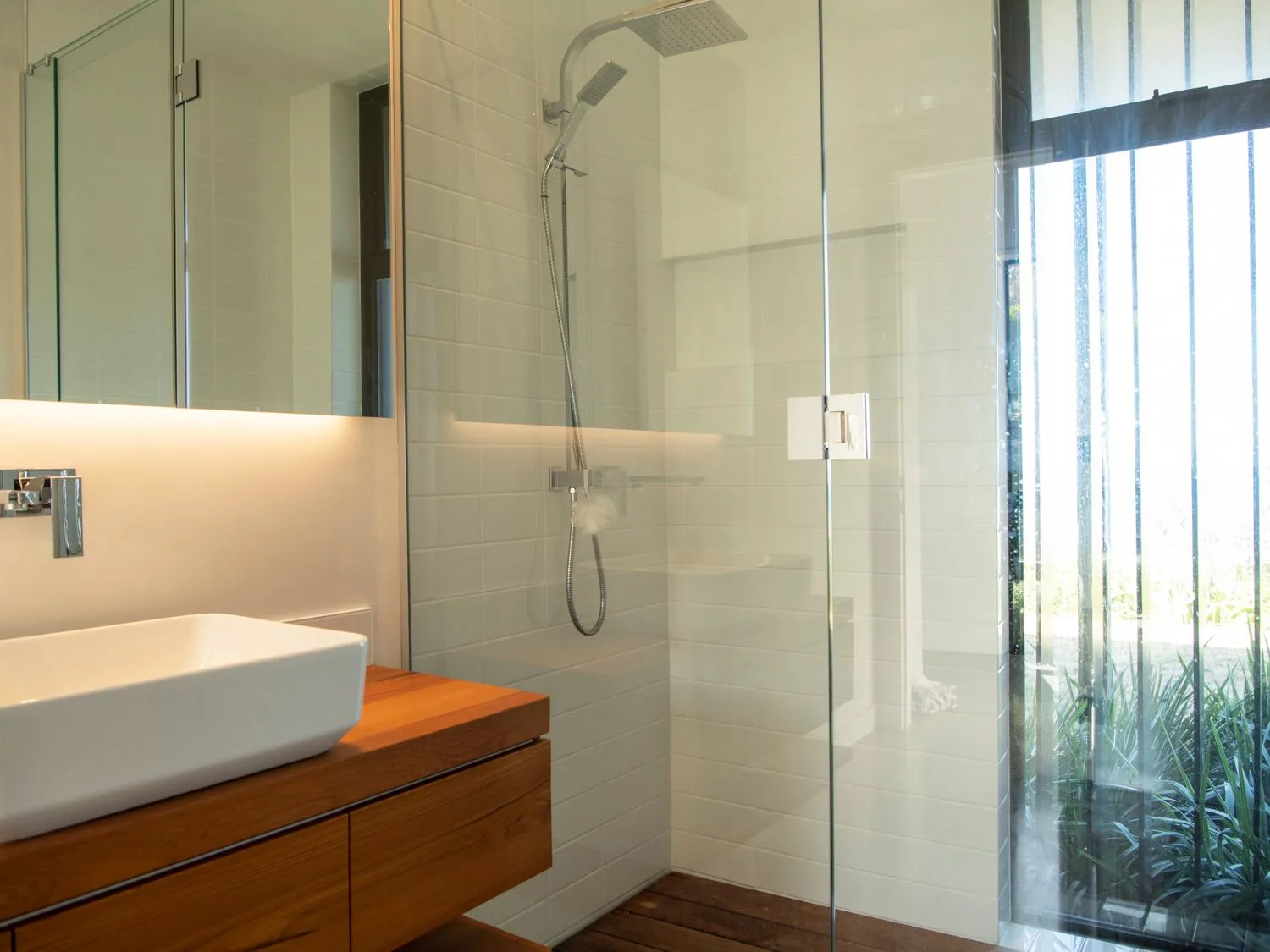 A bathroom with a wooden vanity, white sink, and glass shower.