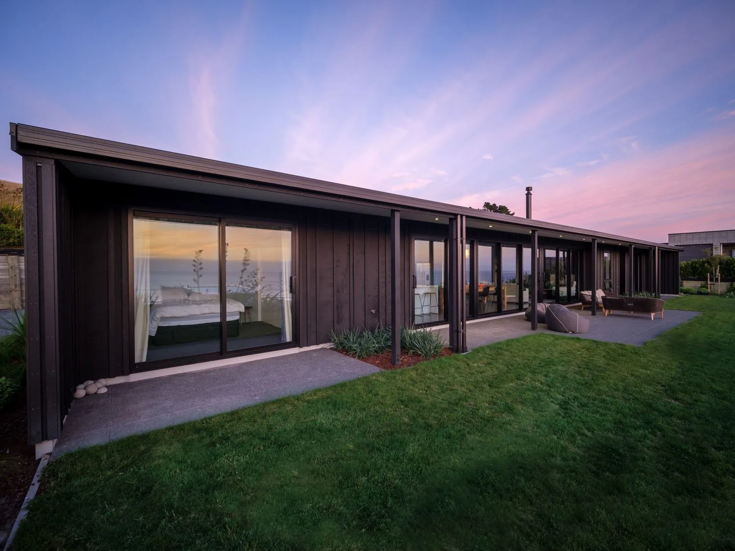 The exterior of a modern single-story house with large sliding glass doors and a grassy lawn at Lightning Ridge Views - Waimarama Holiday Home in Waimarama