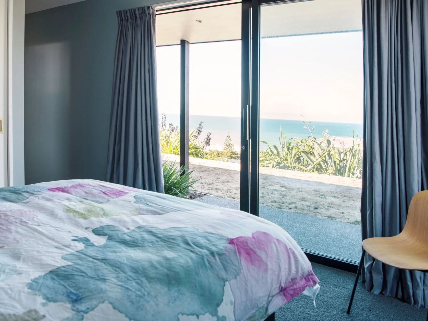 A bedroom with a colorful bedspread beside sliding glass doors and gray curtains.