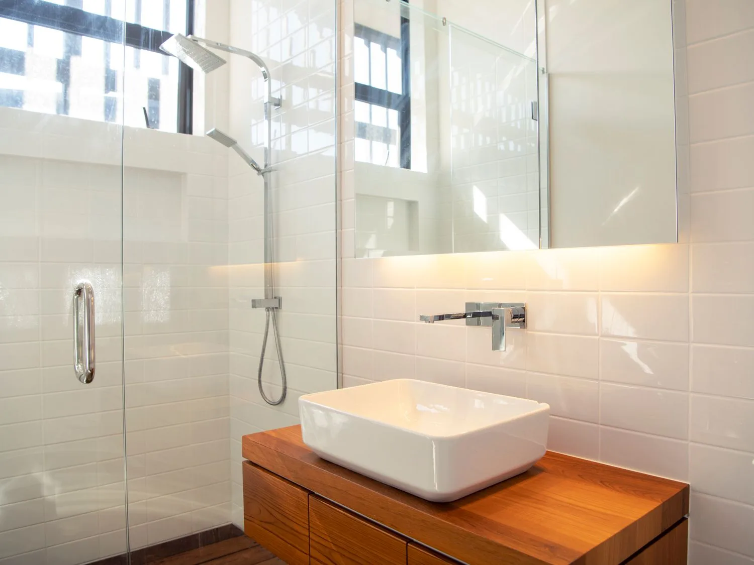 A bright bathroom with a glass shower and a white sink on a wooden vanity.
