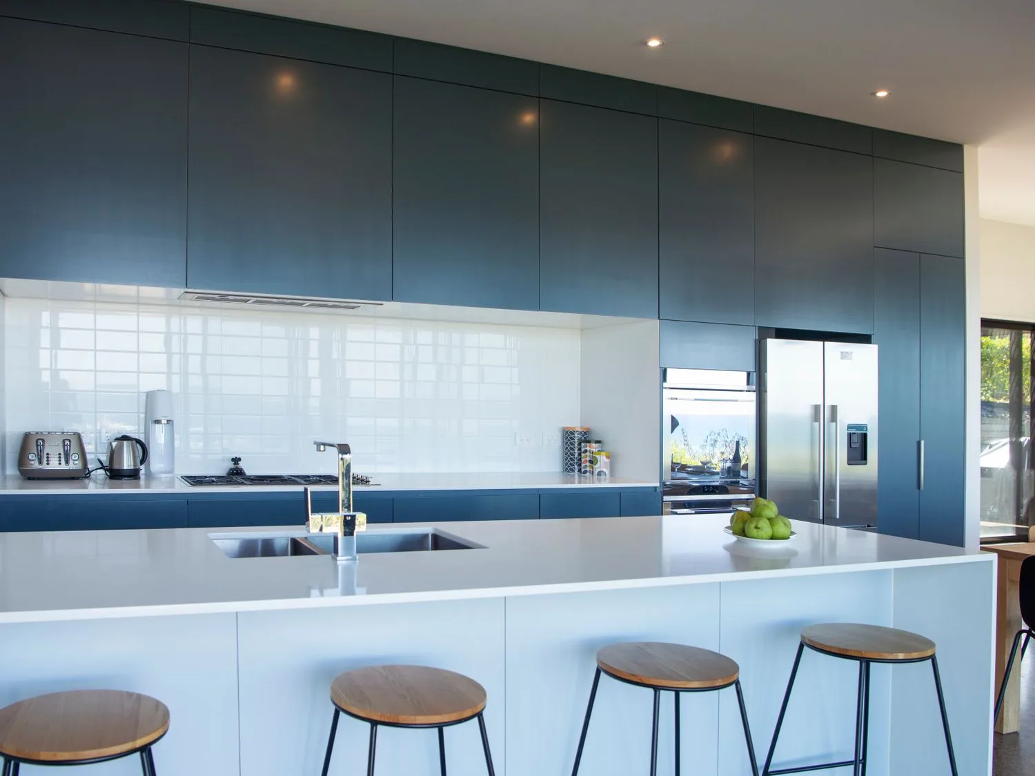 Una cocina con una isla blanca, taburetes de madera y muebles oscuros en Lightning Ridge Views - Waimarama Holiday Home, en Waimarama