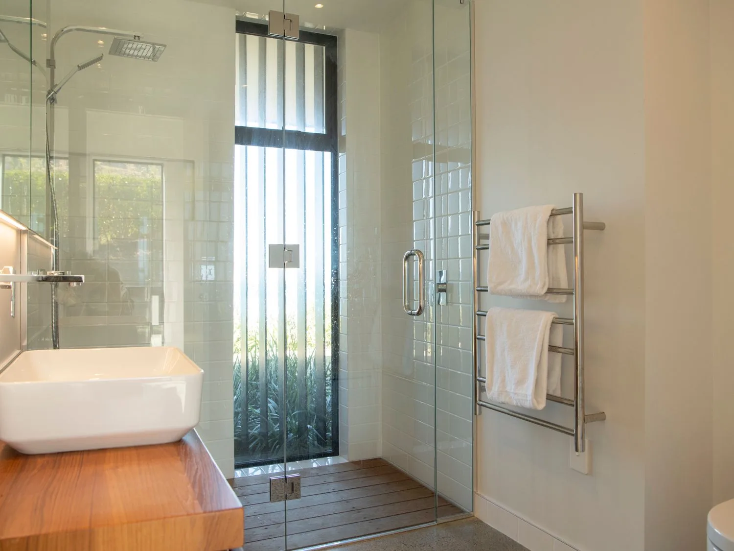 A bathroom with a glass shower, wooden countertop, white sink, and towel rack.