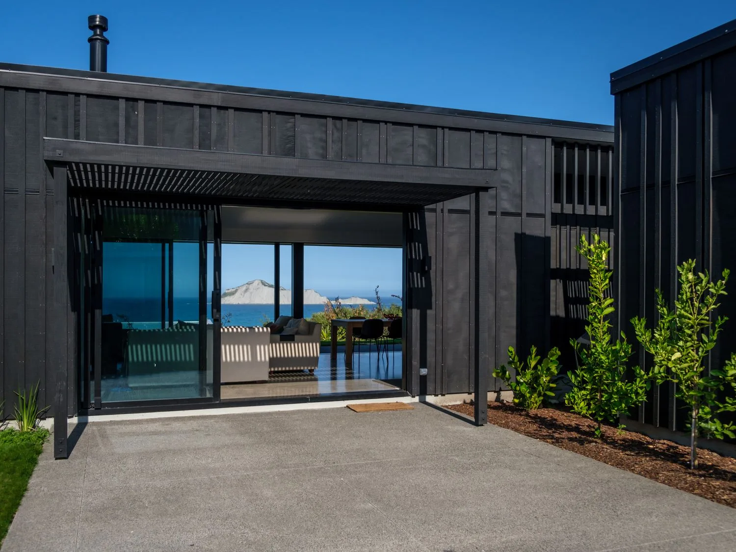 An outside view of a black house with glass sliding doors showing a living room and ocean view at Lightning Ridge Views Waimarama