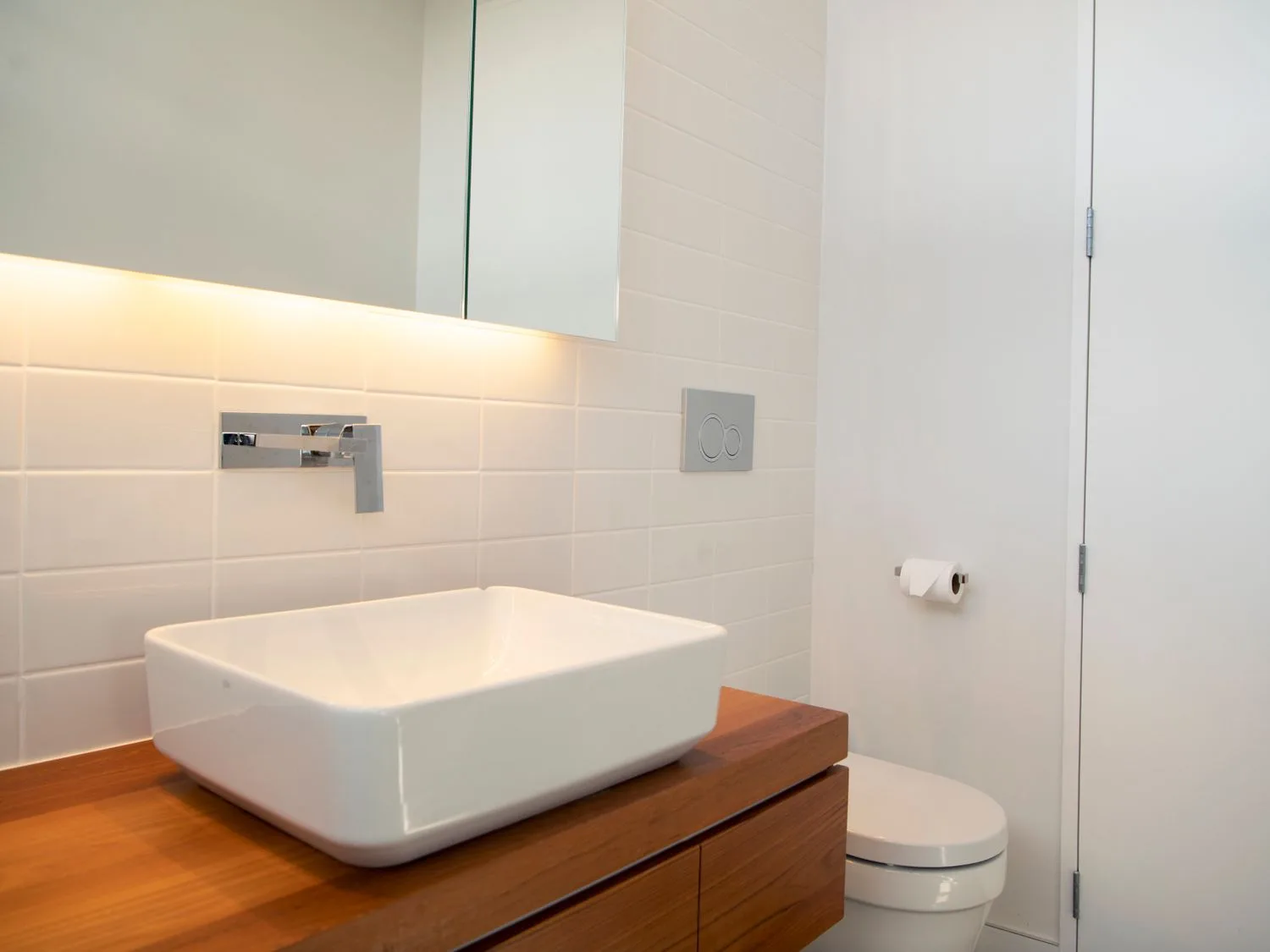 A bathroom with a white vessel sink on a wooden vanity and a toilet.