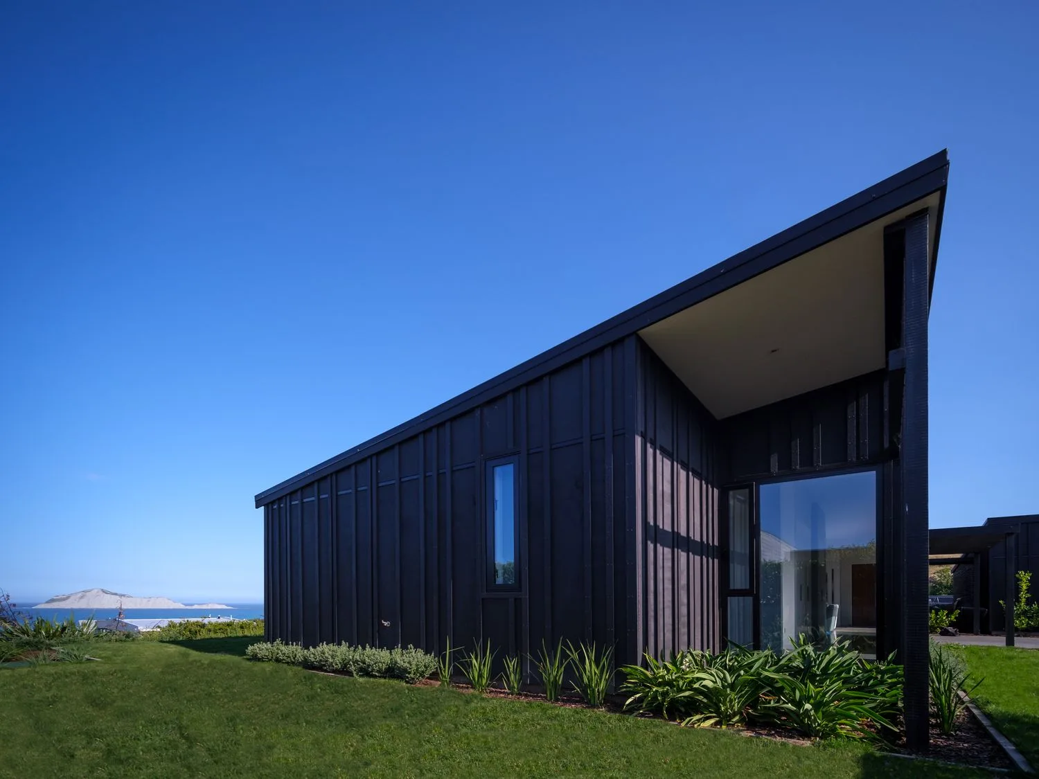 A modern black house with sloped roof and greenery around at Lightning Ridge Views Waimarama Holiday Home in Waimarama
