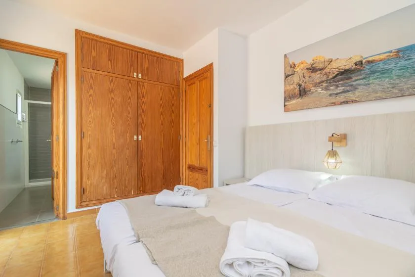 A bedroom with a double bed, folded towels, and a large wooden wardrobe.