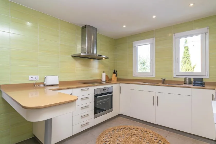 A bright kitchen with light-colored cabinets, tiled walls, and a countertop.