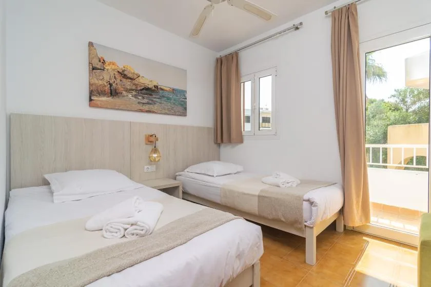 A bedroom with two beds, light bedding, and a balcony door.