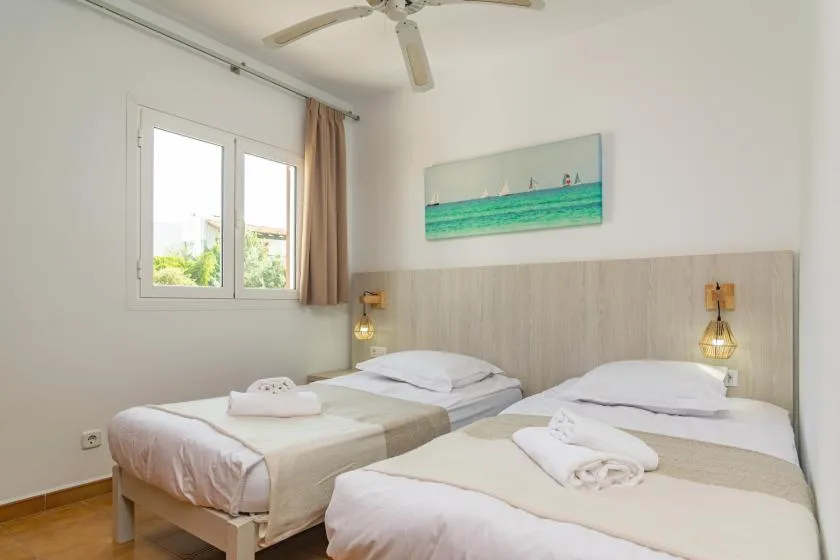 A bedroom with two beds, folded towels, and a window.