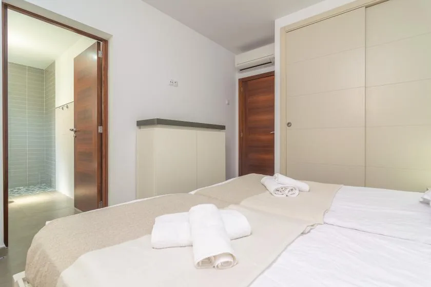 A bedroom with white bedding and folded towels, next to an open bathroom.