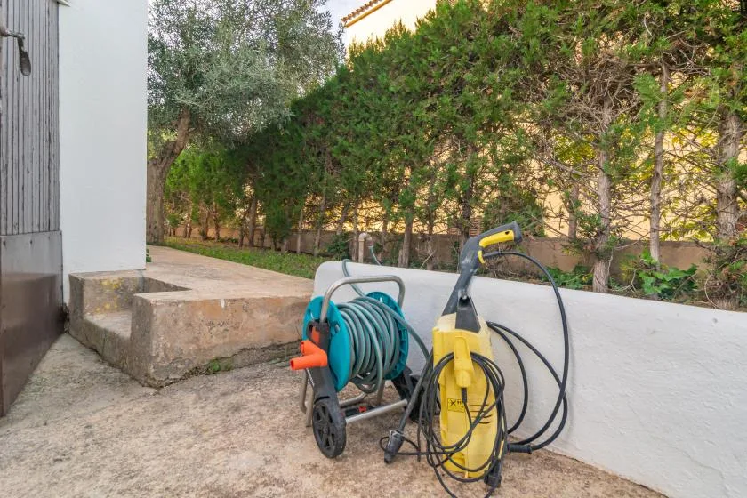 Outdoor area beside a wall with a garden hose reel and pressure washer.