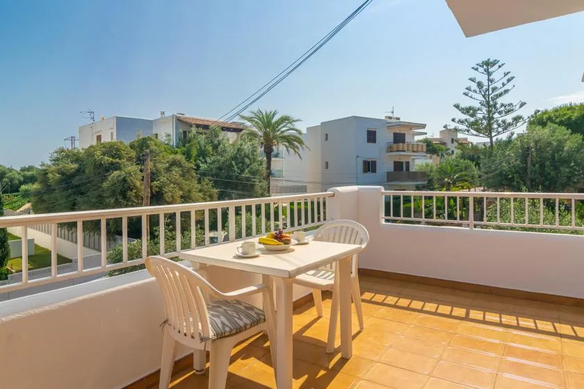A sunny outdoor terrace with a table and seating overlooking nearby buildings and trees.