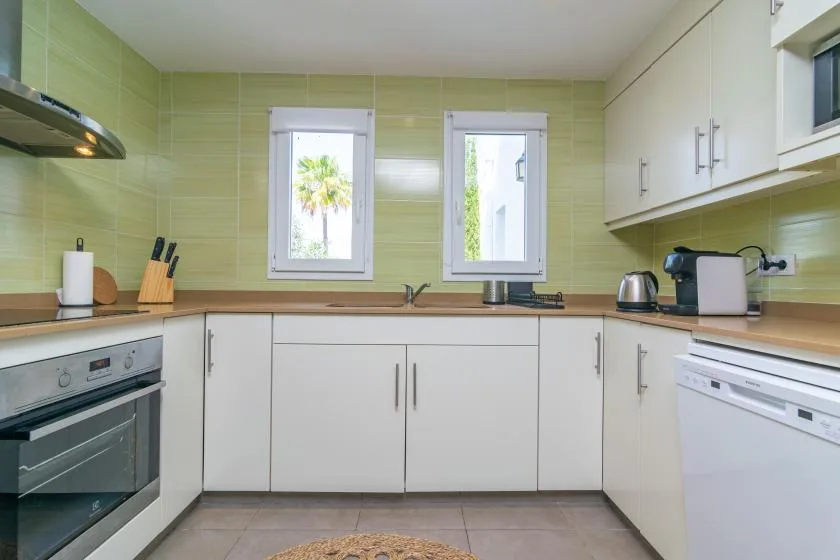 A bright kitchen with pale green tiled walls and white cabinets.