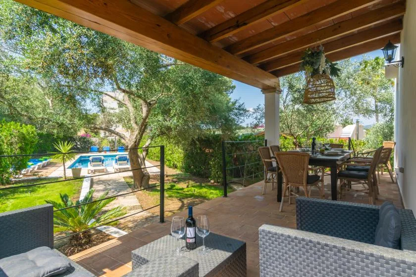 A covered outdoor patio with seating overlooks a garden and swimming pool.