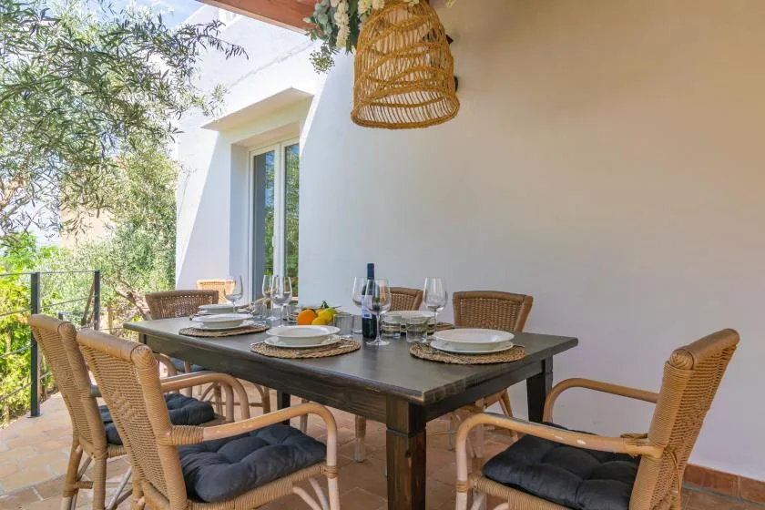 An outdoor dining area has a wooden table set with dishes and wicker seating.
