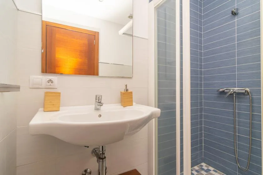 A bathroom with a wall-mounted sink beside a tiled shower.