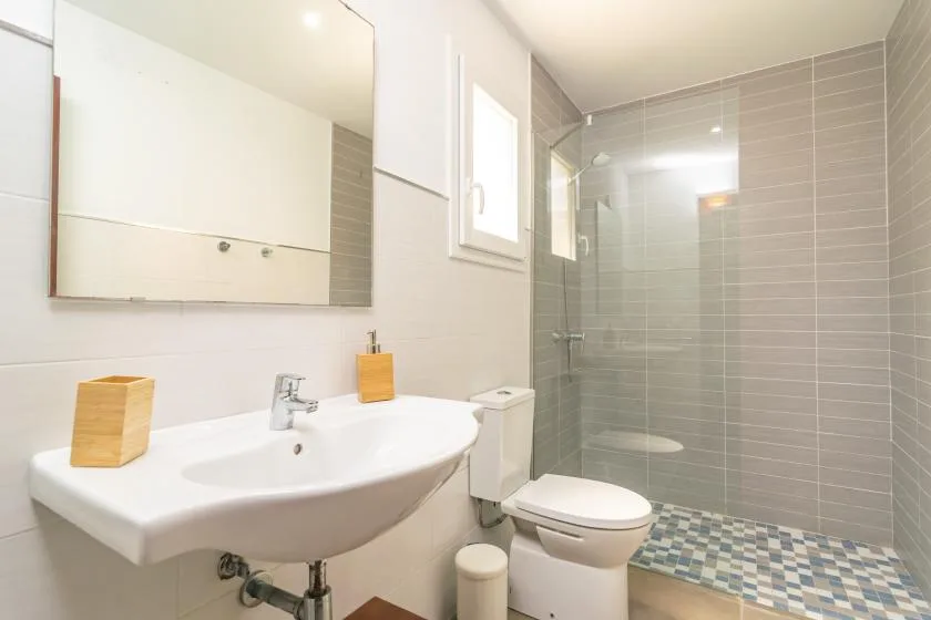 A bright bathroom with a sink, toilet, and tiled shower.
