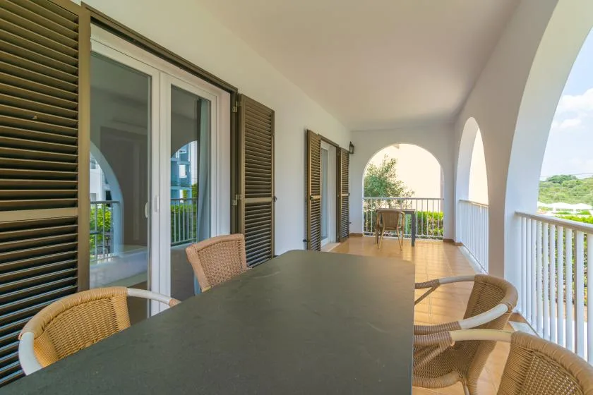 A covered balcony with a long table and seating beside arched openings.