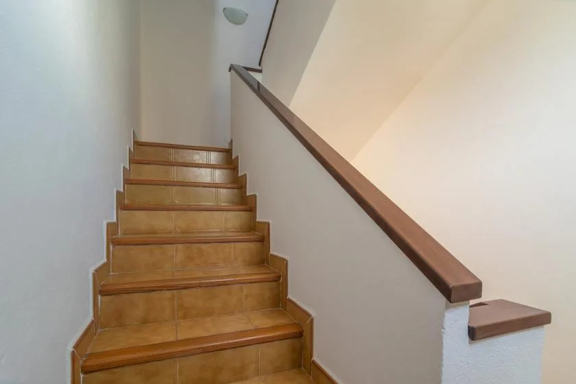 A tiled staircase rises beside a wall with a wooden handrail.