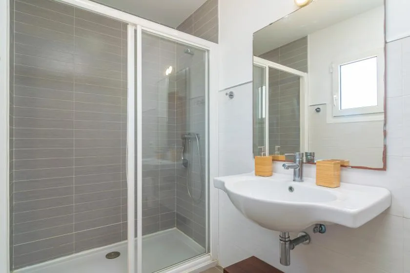 A bathroom with a glass shower, a wall-mounted sink, and a mirror.