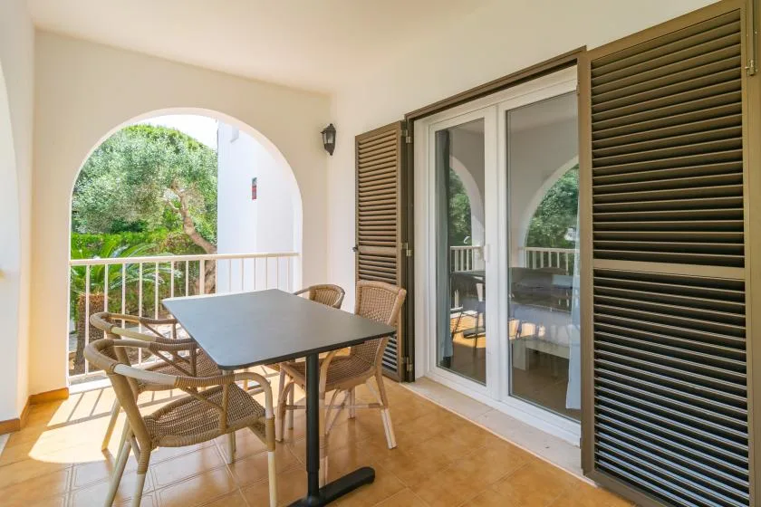 A covered balcony dining area with a table and seating beside sliding glass doors.