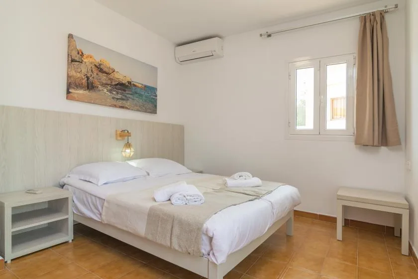 A bright bedroom with a double bed, bedside table, and window.