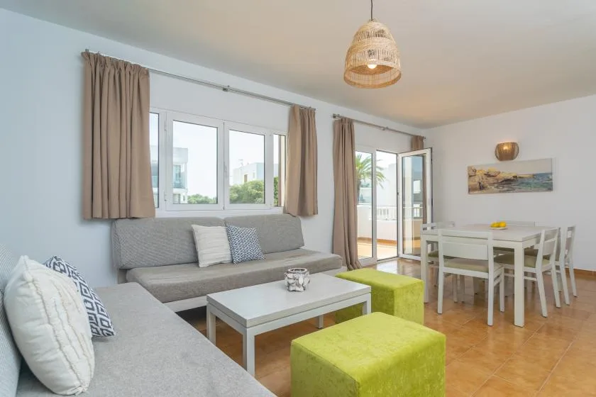 A bright living and dining area with seating, green ottomans, and a white dining table.