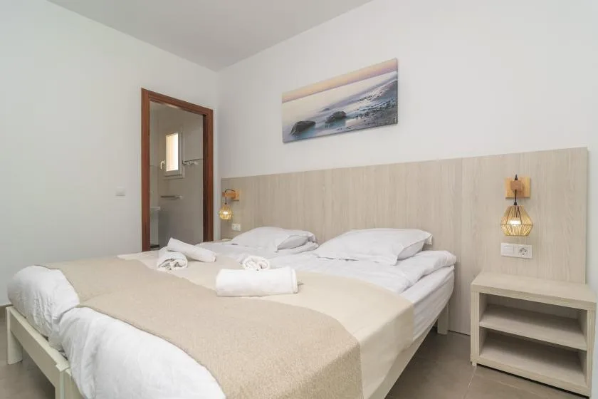 A bedroom with a double bed, pale bedding, and wall-mounted bedside lights.