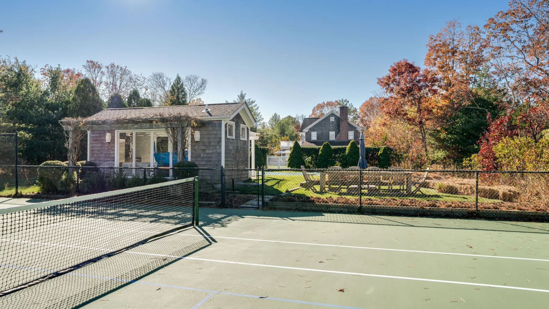 Una cancha de tenis al aire libre junto a un edificio pequeño y árboles otoñales.